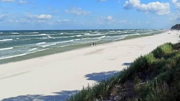 Ein Strand mit Wellen, blauem Himmel und ein paar Spaziergängern.