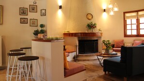 A living room with a fireplace, a sofa, a coffee table, and a bar area with stools. - Gravanis Resort Luxury Villa with Private Pool in 30Acre Olive Grove near Athens (Sykamino)