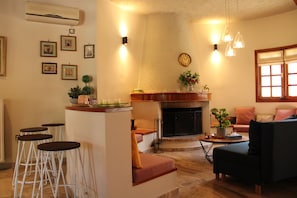 A living room with a fireplace, a sofa, a coffee table, and a bar area with stools. - Gravanis Resort Luxury Villa with Private Pool in 30Acre Olive Grove near Athens (Sykamino)