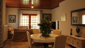 A dining area with a round table, chairs, a vase with flowers, and a television in the background. - Gravanis Resort Luxury Villa with Private Pool in 30Acre Olive Grove near Athens (Sykamino)