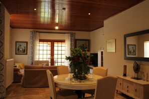 A dining area with a round table, chairs, a vase with flowers, and a television in the background. - Gravanis Resort Luxury Villa with Private Pool in 30Acre Olive Grove near Athens (Sykamino)