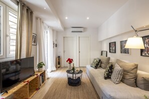 A living room with a flat-screen TV, a sofa, a coffee table with a vase and a bottle, and a wall-mounted air conditioner. - Roncaglia, 27 - Comfort & Character (Milano)
