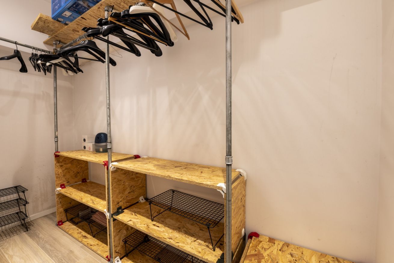 A room with three wooden shelves, metal wire shelves, and a metal pole.