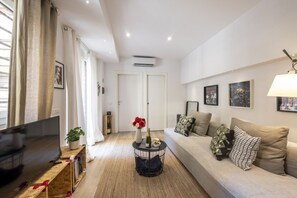 A modern living room with a flat-screen TV, a round coffee table with a bottle and flowers, a sofa with patterned cushions, and framed pictures on the wall. - Roncaglia, 27 - Comfort & Character (Milano)