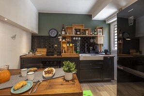 A modern kitchen with a brick backsplash, wooden shelves, and a dining area with a table set for two. - Roncaglia, 27 - Comfort & Character (Milano)