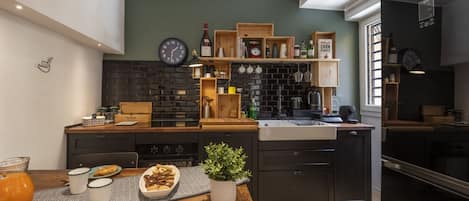 A modern kitchen with a brick backsplash, wooden shelves, and a dining area with a table set for two.