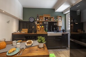 A modern kitchen with a brick backsplash, wooden shelves, and a dining area with a table set for two. - Roncaglia, 27 - Comfort & Character (Milano)