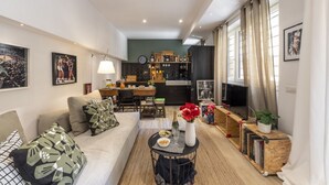 A modern living room with a sofa, coffee table, and a TV. There is a kitchen in the background with a dining area. - Roncaglia, 27 - Comfort & Character (Milano)
