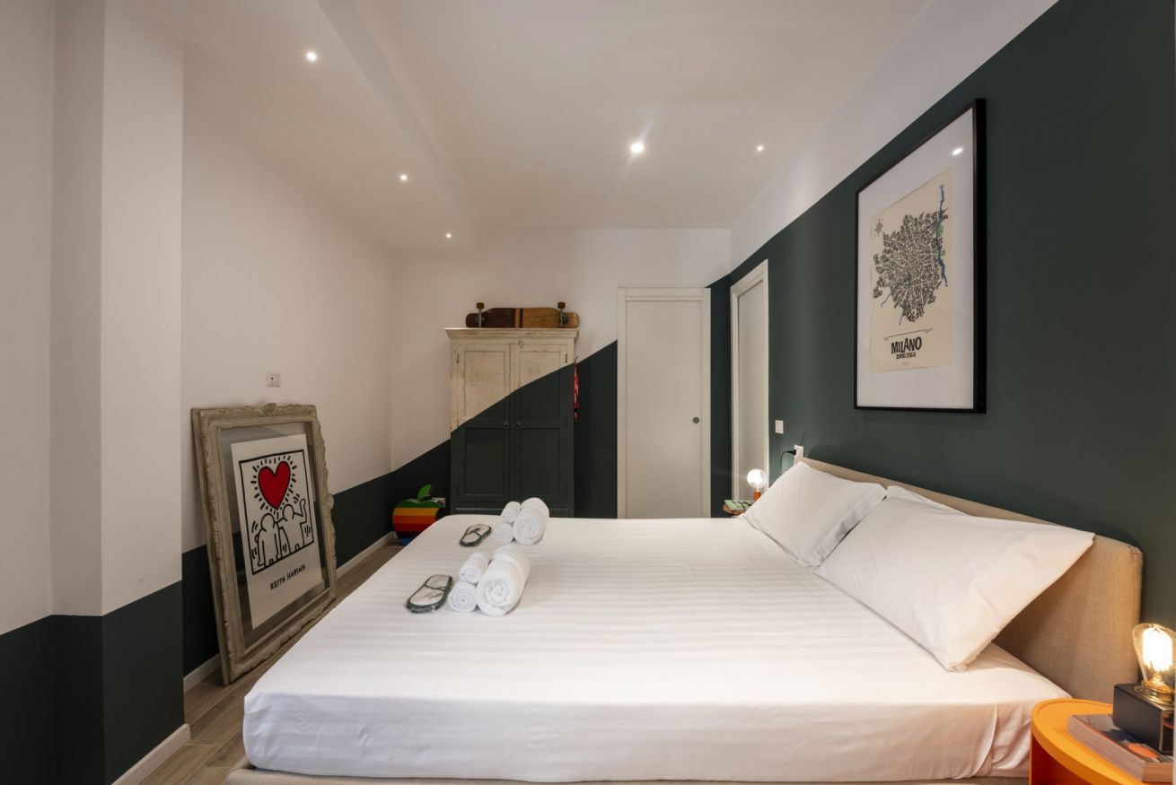 Una habitación de hotel con una cama, un cuadro enmarcado, una mesita de noche y una escalera.