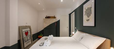 Una habitación de hotel con una cama, un cuadro enmarcado, una mesita de noche y una escalera.
