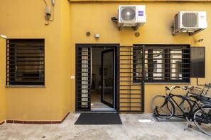 A yellow building with a black gate, air conditioning units, and bicycles parked outside. - Roncaglia, 27 - Comfort & Character (Milano)