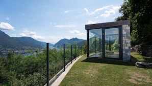 Een modern gebouw van glas met stenen accenten, met uitzicht op een bergachtig landschap en een waterpartij.