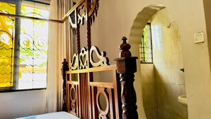 Ein Schlafzimmer mit Bett, einem Fenster mit Vorhängen, einem Badezimmer mit Waschbecken und Dusche sowie einer dekorativen Holzabtrennung.
