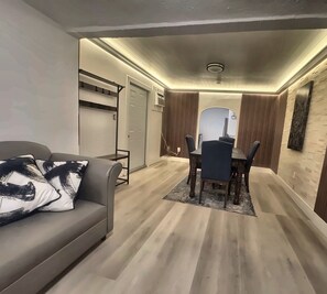 Ein modernes Wohnzimmer mit einer Couch, einem Esstisch mit Stühlen und einer Küchenzeile im Hintergrund.