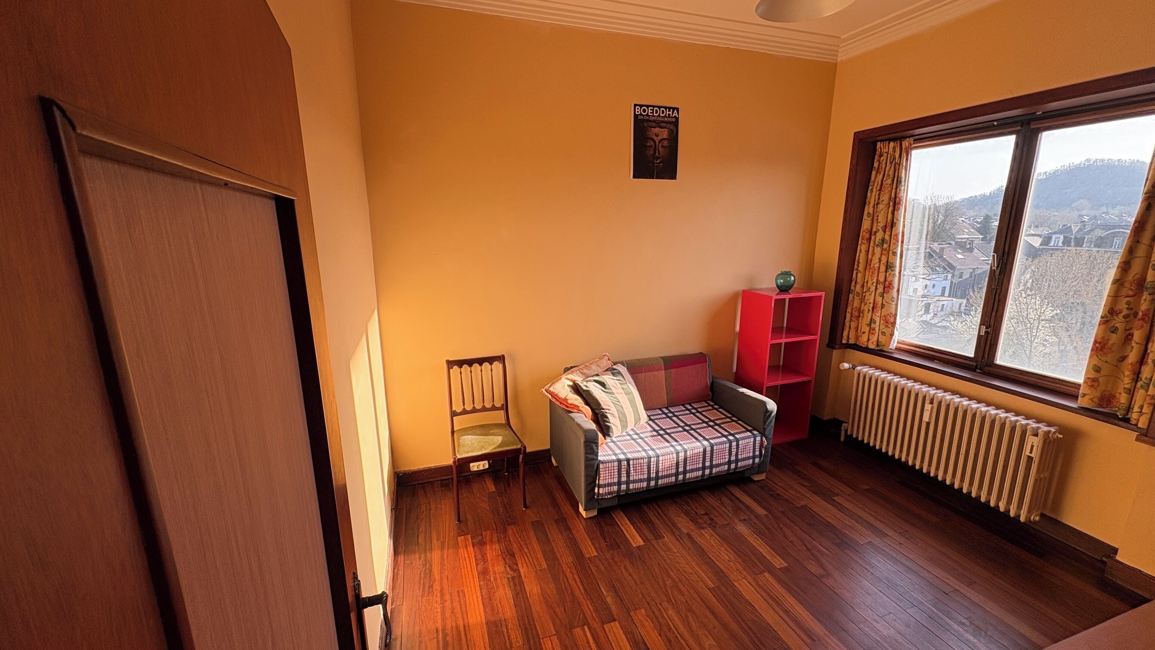 Une pièce avec un plancher en bois, un canapé, une chaise, un radiateur et une fenêtre donnant sur un beau paysage.