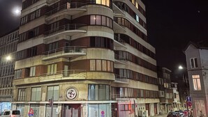 Un edificio de varios pisos con balcones, un escaparate visible y una calle en la parte delantera.