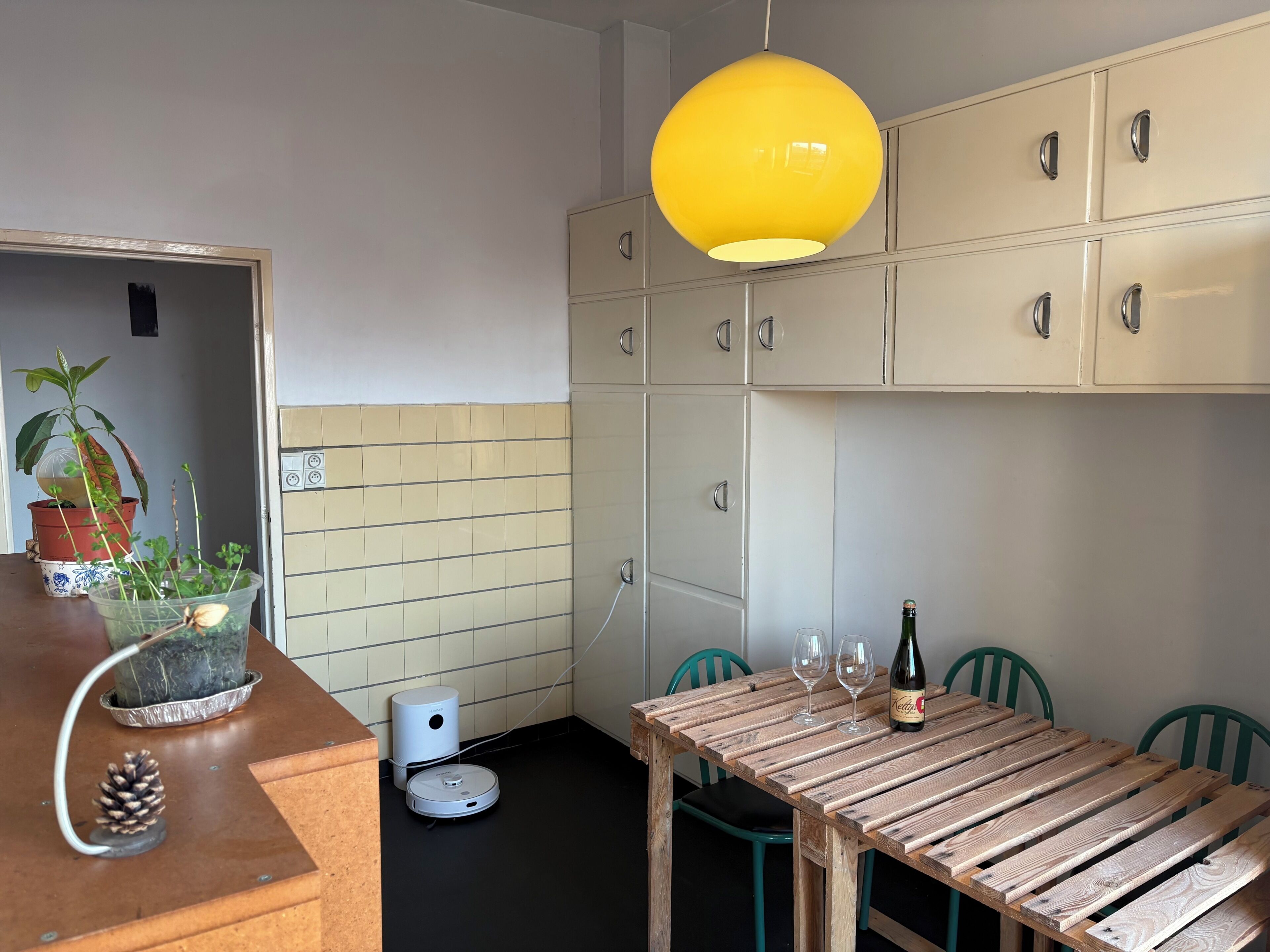 Une cuisine avec une table à manger, des chaises, un luminaire jaune suspendu et des placards.