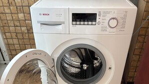 Una lavadora blanca de Bosch con panel de control, puerta abierta y piso de baldosas.