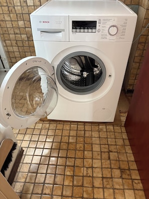 Une machine à laver Bosch blanche, avec un panneau de commande, une porte ouverte et un sol carrelé.