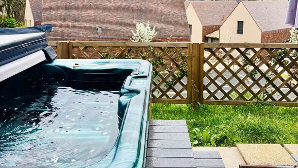 A hot tub in a backyard with a wooden fence, a table, and houses in the background. - Parenthèse Soleil-Terrace-Parking-Historic heart (Sarlat-la-Canéda)