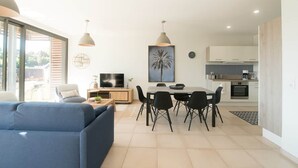 A modern living room with a sofa, dining table, chairs, and a TV. - Parenthèse Soleil-Terrace-Parking-Historic heart (Sarlat-la-Canéda)