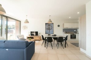 A modern living room with a sofa, dining table, chairs, and a TV. - Parenthèse Soleil-Terrace-Parking-Historic heart (Sarlat-la-Canéda)