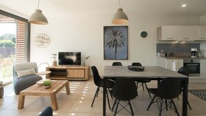 A modern living room with a TV, dining table, chairs, and artwork on the wall. - Parenthèse Soleil-Terrace-Parking-Historic heart (Sarlat-la-Canéda)
