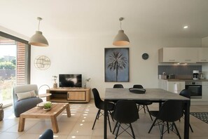 A modern living room with a TV, dining table, chairs, and artwork on the wall. - Parenthèse Soleil-Terrace-Parking-Historic heart (Sarlat-la-Canéda)