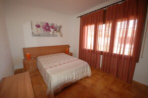 Quarto com cama de madeira, mesa de cabeceira, luminária na parede e janela com cortinas.