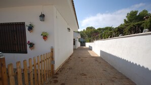 A narrow paved pathway flanked by white walls, wooden fence, and hanging flower pots. - SAONA VILLAS (VN FARNO): villa sleeps 6, private pool, wifi, air-conditioning (Les Tres Cales)