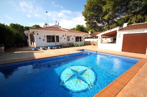 Uma piscina com padrão de estrelas, um edifício branco com telhado vermelho e uma cerca de madeira.