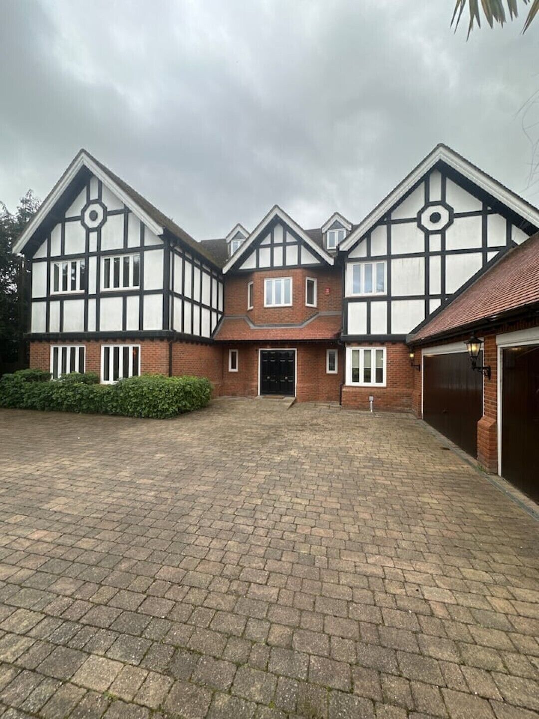 Een huis in Tudorstijl met twee verdiepingen, een gevel van baksteen, meerdere ramen en een verharde oprit.