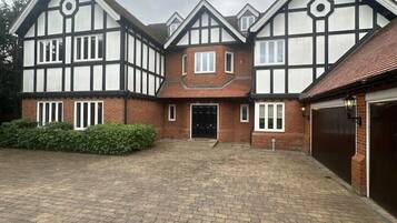 Een huis in Tudorstijl met twee verdiepingen, een gevel van baksteen, meerdere ramen en een verharde oprit.