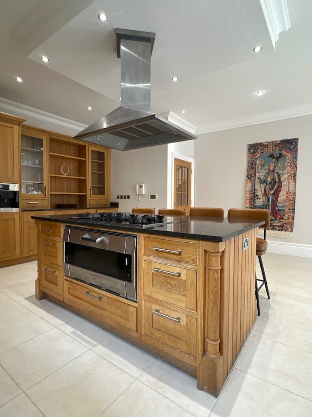 A modern kitchen with an island, built-in oven, and stainless steel range hood.