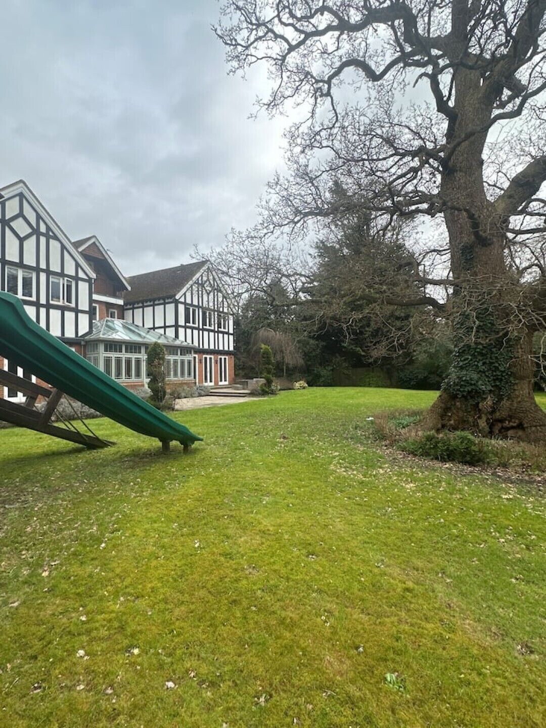 Un parco con uno scivolo verde, un albero grande e un edificio tradizionale con veranda in vetro.