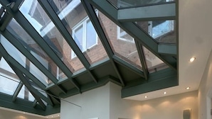 Un interior amplio con techo alto, tragaluz y una puerta central que da a otra habitación.