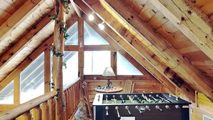 Ein gemütliches Dachzimmer mit Holzbalken, einem Kicker und großen Fenstern.