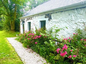 Een wit stenen gebouw met een grindpad en roze bloemen.