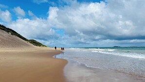 En strand med bred sandstrand, blide bølger og klar himmel.