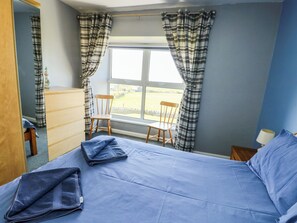 A bedroom with a bed, two wooden chairs, a dresser, and a window with curtains. - Bodlasan Groes House (Holyhead)
