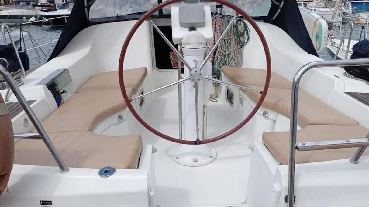 Interior de un barco con timón, asientos acolchados y panel de control.