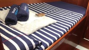 Una cama pequeña y estrecha con una colcha azul y blanca a rayas, dos toallas enrolladas y una almohada blanca.