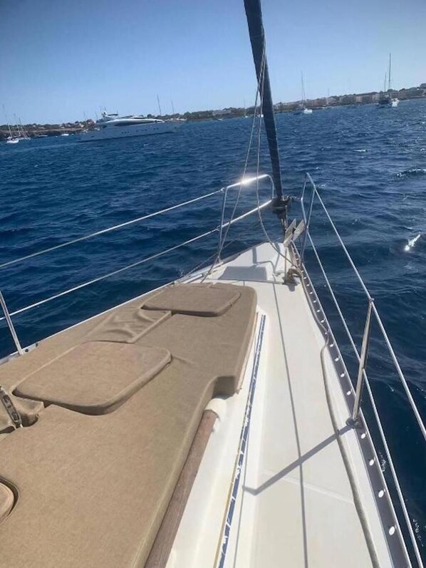 A sailboat's deck with a cushioned area, metal railings, and a clear view of the water.