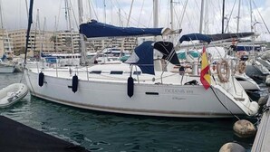 Un puerto deportivo con barcos amarrados, incluyendo un yate blanco llamado 'OCEANIS 393' con una capota azul y una bandera roja.