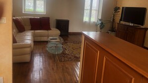 A living room with a sofa, a glass coffee table, a wooden cabinet, and a television. - Belle Maison dans une ancienne école (Chemille-en-Anjou)