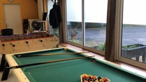 A pool table with balls, a foosball table, and a window with a view of the water. - Belle Maison dans une ancienne école (Chemille-en-Anjou)