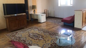 A living room with a TV, a desk, a chair, a sofa, a glass coffee table, and a patterned rug. - Belle Maison dans une ancienne école (Chemille-en-Anjou)