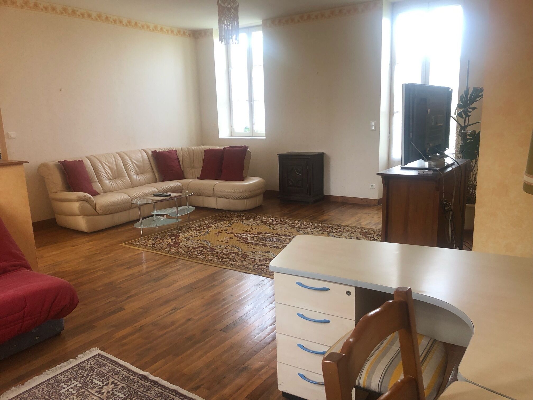 A living room with a beige sectional sofa, a small coffee table, a wooden cabinet, and a television.