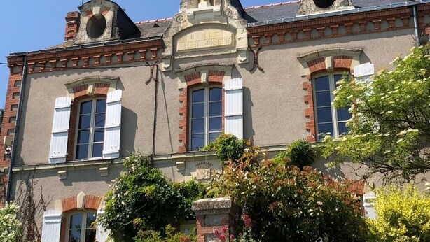 A historic building with a central tower, arched windows, and a statue on top. - Belle Maison dans une ancienne école (Chemille-en-Anjou)