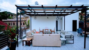 A rooftop patio with a pergola, a sofa, a dining table with chairs, and potted plants. - Juru House Rentals  (Kigali)
